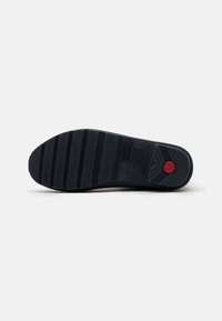 Semelle de chaussure en caoutchouc noir avec une surface texturée, présentant des rainures horizontales et un accent rouge près du talon. Conception durable et antidérapante.