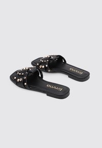 Sandales à glissière noires en matériau synthétique, ornées de clous en or rose, avec un design à bout ouvert, une semelle plate et un logo en relief sur la semelle intérieure.