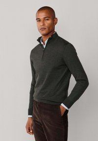 Dunkelgrauer Reißverschluss-Pullover aus weichem Strickstoff, mit einem hohen Kragen und gerippten Bündchen, über einem hellblauen Hemd mit Kragen getragen.