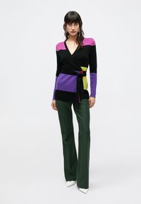 Juodas megztinis su violetiniais, rožiniais ir žaliais spalvų blokais. Turi diržu juosiamą liemenį ir ilgus rankovius. Derinamas su žaliais platėjančiais kelnėmis.