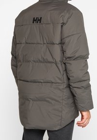 Giacca a vento, grigia, con cuciture orizzontali, colletto alto e logo sul retro. Presenta una texture liscia e una vestibilità aderente.