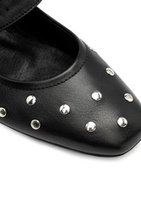 Zapato de cuero negro con punta afilada, adornado con tachuelas plateadas en la parte delantera. El interior parece suave y texturizado.