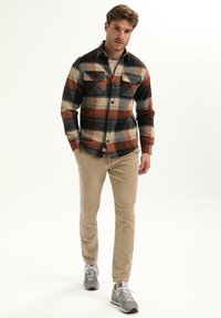 Geruite flanellen shirt in marineblauw, oranje en crème. Heeft borstzakken en knoopsluiting. Gecombineerd met beige corduroypantalon en grijze sneakers.