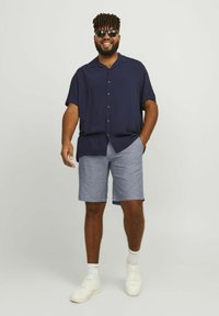 Chemise à manches courtes bleu marine avec boutons, shorts bleus clairs, baskets blanches et lunettes de soleil ; coupe décontractée avec une texture douce et un design décontracté.