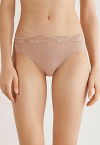 Beige ondergoed met kantafwerking, geribd met een golvende taille en delicate details langs de randen, ontworpen voor een aansluitende pasvorm.
