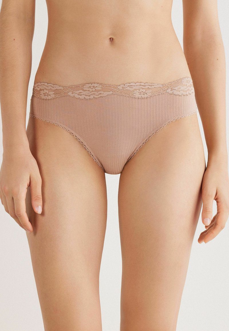 Beige ondergoed met kantafwerking, geribd met een golvende taille en delicate details langs de randen, ontworpen voor een aansluitende pasvorm.