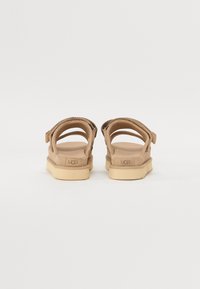 Bruine suède sandalen met verstelbare band, gevoerde zolen en rubberen buitenzool. Kenmerkt zich door UGG-branding op de hiel.