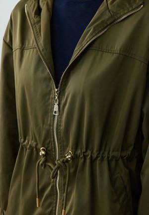 Giacca a vento verde oliva con chiusura a zip, vita con cordino e hardware in tono oro, realizzata in un tessuto leggero e liscio.