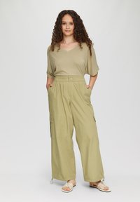 Khaki cargobroek met wijde benen en zijzakken, gecombineerd met een lichtolijfkleurig T-shirt met V-hals en korte mouwen. Platte sandalen maken de outfit compleet.