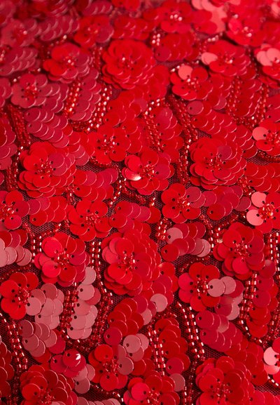 Tissu en sequins rouges présentant des motifs floraux avec des sequins ronds brillants et une texture en filet contrastante. Richement superposé pour un look vibrant.