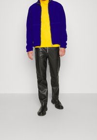 Fioletowa kurtka na zamek, żółty dzianinowy golf, czarne skórzane spodnie oraz czarne botki za kostkę. Teksturowana dzianina i gładka skórzana tkanina.