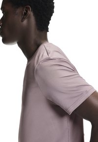 Vaaleanpunainen tekninen lyhythihainen paita, jossa on koristeltu kangaspinta, pyöreä pääntie ja hillitty logopainatus rinnassa.