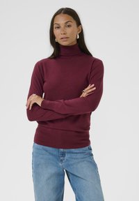 Burgundy-coloured kauluspusero valmistettu pehmeästä kankaasta, jossa on pitkät hihat ja joustavat hihansuut sekä helma, yhdistettynä vaaleansinisiin farkkuihin.