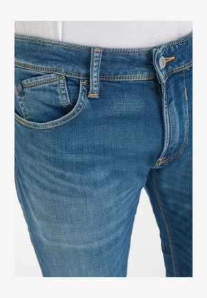 Blauwe spijkerbroek met een klassiek ontwerp met vijf zakken, met contrasterende gele stiksels en een gladde textuur. Knopen als sluiting bij de taille.