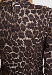 Leopardenmusterkleid mit weicher Textur, das braune und schwarze Flecken auf einem hellen Hintergrund zeigt und einen Reißverschluss auf der Rückseite sowie ein Etikett hat.