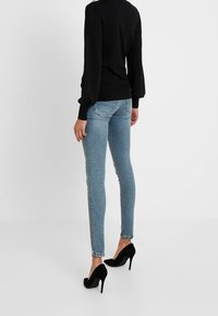 Czarna bluzka z długim rękawem, dopasowana w talii, średnio niebieskie obcisłe dżinsy, szczegółowe przeszycia, postrzępiony dół oraz czarne buty na wysokim obcasie.