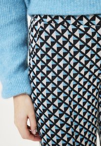 Gebreide, lichtblauwe trui gecombineerd met patroonrijke, high-waisted broek met zwarte, witte en lichtblauwe driehoeken in een geometrisch ontwerp.