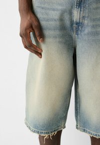 Pantalones cortos de mezclilla en azul claro con un acabado desgastado y dobladillos deshilachados. Primer plano que muestra la textura y la variación de color en la tela.