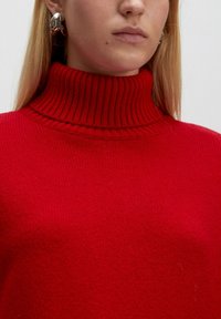 Roter gerippter Rollkragenpullover aus gestricktem Stoff mit hohem Kragen und strukturierter Oberfläche ohne sichtbare Muster oder Akzente.