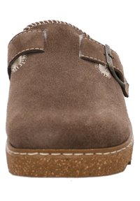 Chaussure à enfiler en cuir suédé marron avec un bout rond, accent en boucle en métal et semelle en liège texturée. Présente des coutures visibles le long des bords.