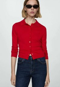 Cardigan rosso con collo, maniche lunghe e chiusura con bottoni. Realizzato in materiale morbido, presenta una forma aderente e una trama a coste sui polsini.
