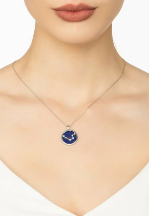 Silver necklace featuring a circular pendant with a navy blue background and white constellation design. Chain is thin and simple.