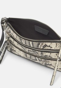 Sac à main imprimé serpent en noir et blanc avec trois compartiments zippés, une surface texturée et une bandoulière amovible. L'intérieur est en tissu noir.