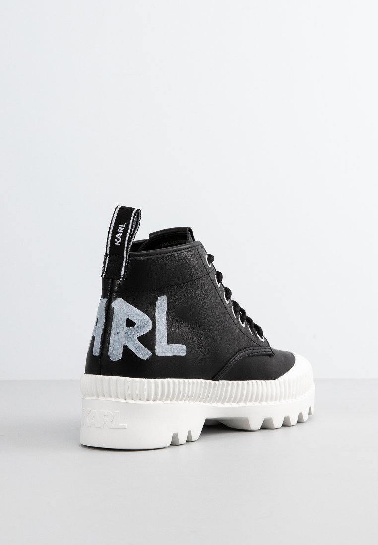 Bottines en cuir noir avec semelle en caoutchouc épaisse blanche. Comprend une languette au talon avec logo et texte peint en bleu sur le côté.