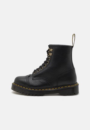 Bottes en cuir noir à mi-mollet avec une finition texturée, bout rond, œillets dorés, surpiqûres jaunes sur la semelle et une languette à l'arrière.