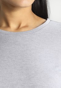 Graues T-Shirt mit rundem Ausschnitt aus weichem Stoff. Es zeichnet sich durch eine glatte Textur mit sichtbaren Nähten am Kragen und an den Schulternähten aus.