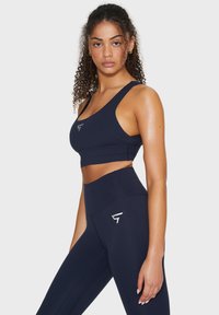 Set di reggiseno sportivo blu navy e leggings a vita alta realizzati in tessuto elasticizzato. Presenta un accento con logo. Texture liscia con un design aderente.