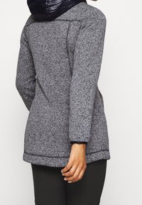 Giacca a maglia grigia con cappuccio imbottito blu navy, maniche lunghe e tasche laterali. Tessuto testurizzato con dettagli a contrasto sui polsini e sull'orlo.