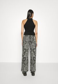 Černý žebrovaný halter top spárovaný se širokými šedými kalhotami s propracovanými černobílými paisley vzory, nošený s masivními černými kozačkami.