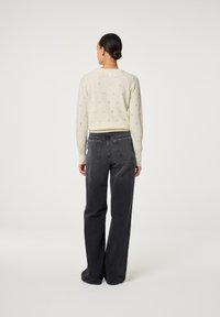 Helles Cremefarbenes Sweater mit kleinen schwarzen Punkten, kombiniert mit dunkelgrauen, weit geschnittenen Jeans mit doppelten Taschen. Weiche Textur, lässiges Design.