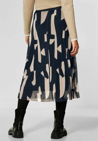 Gonna midi plissettata con base blu navy e motivi astratti beige, realizzata in tessuto leggero, abbinata a stivali neri alla caviglia.