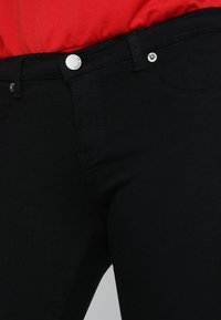 Jeans negros hechos de denim con una textura suave. Las características incluyen botones plateados y un diseño estándar de cinco bolsillos.