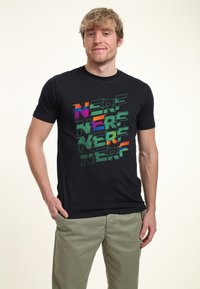 Sort bomulds t-shirt med en flerfarvet grafik af ordet "NERF" i forskellige skrifttyper og stilarter, sat mod en neutral baggrund.