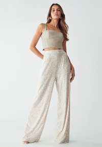 Top beige cropped con scollatura quadrata; pantaloni a gamba larga lucidi coperti di paillettes argentate; texture liscia; design complessivo elegante.
