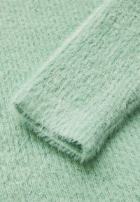 Light green knitted fabric with a soft, fluffy texture, featuring a diagonal rib pattern and a folded edge for a finished look.