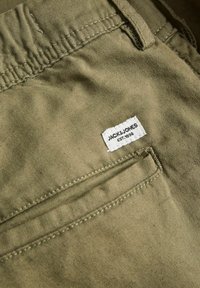 Gros plan sur la poche d'un pantalon en tissu kaki avec une petite étiquette blanche portant la mention Jack & Jones EST. 1990 cousue au-dessus de la couture de la poche.