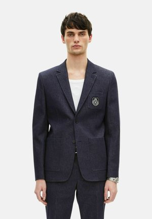 Marineblazer aus strukturiertem Stoff mit einem Revers, zwei Fronttaschen, einer einreihigen Knopfclosure und einem Patch mit Emblem auf der linken Brust.