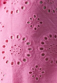Pink fabric featuring embroidered floral patterns with cutouts. The texture is smooth, with detailed stitching around circular designs.