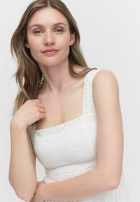 Witte bloemen geborduurde jurk met vierkante halslijn en dunne bandjes. Bevat kantdetails langs het lijfje. Soepele, lichte stof.