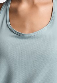 Canotta atletica azzurra chiara con una texture liscia e rigata, scollatura rotonda e cuciture rinforzate. Il tessuto sembra morbido e traspirante.
