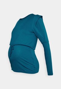 Teal långärmad graviditetsblus med dragsko i midjan, rund halsringning och figurnära design, tillverkad av mjukt bomullsblandningsmaterial.