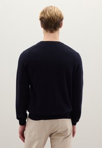Marineblauer Strickpullover mit langen Ärmeln und rundem Ausschnitt, mit geripptem Saum. Der Rücken des Models ist vor einem neutralen Hintergrund zu sehen.
