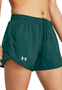 Närbild av en person som bär mörkgröna Under Armour-träningsshorts med elastisk midja och snörning.