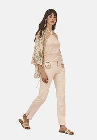 Kimono ligero con estampado floral sobre una blusa ajustada sin mangas y pantalones ligeros y entallados. Dobladillo asimétrico y sandalias con tiras.