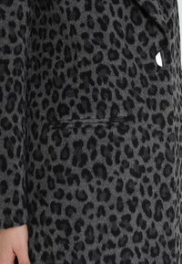 Kabát s leopardím vzorem v šedé a černé barvě, vyrobený z měkké texturované tkaniny. Má náprsní kapsu a zkosené klopy.