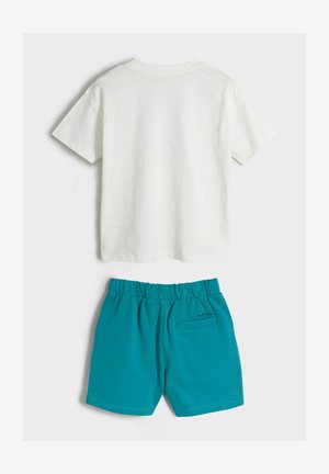 Fehér pamut póló rövid ujjal és kerek nyakkal, türkiz pamut rövidnadrággal párosítva, amely rugalmas derékrésszel és hátsó zsebbel rendelkezik.